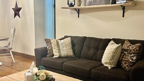 A living room with a dark brown sofa, a wooden coffee table, and a patterned rug. There are two wall-mounted shelves with decorative items. - 🏡Little Bear Cabin In Helen🐻 (Helen)