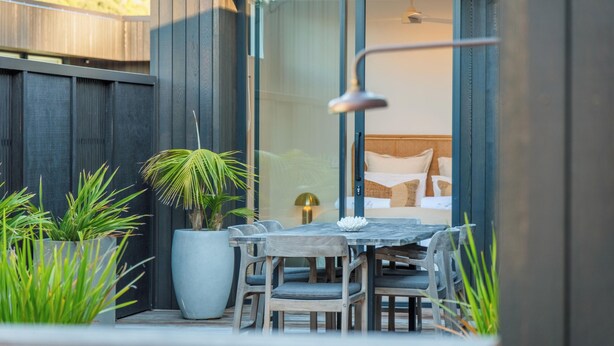 A modern outdoor patio with a wooden table and chairs, surrounded by potted plants.