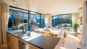 A modern kitchen with a large island, dining area with a table and chairs, and a view of the outside through large windows.