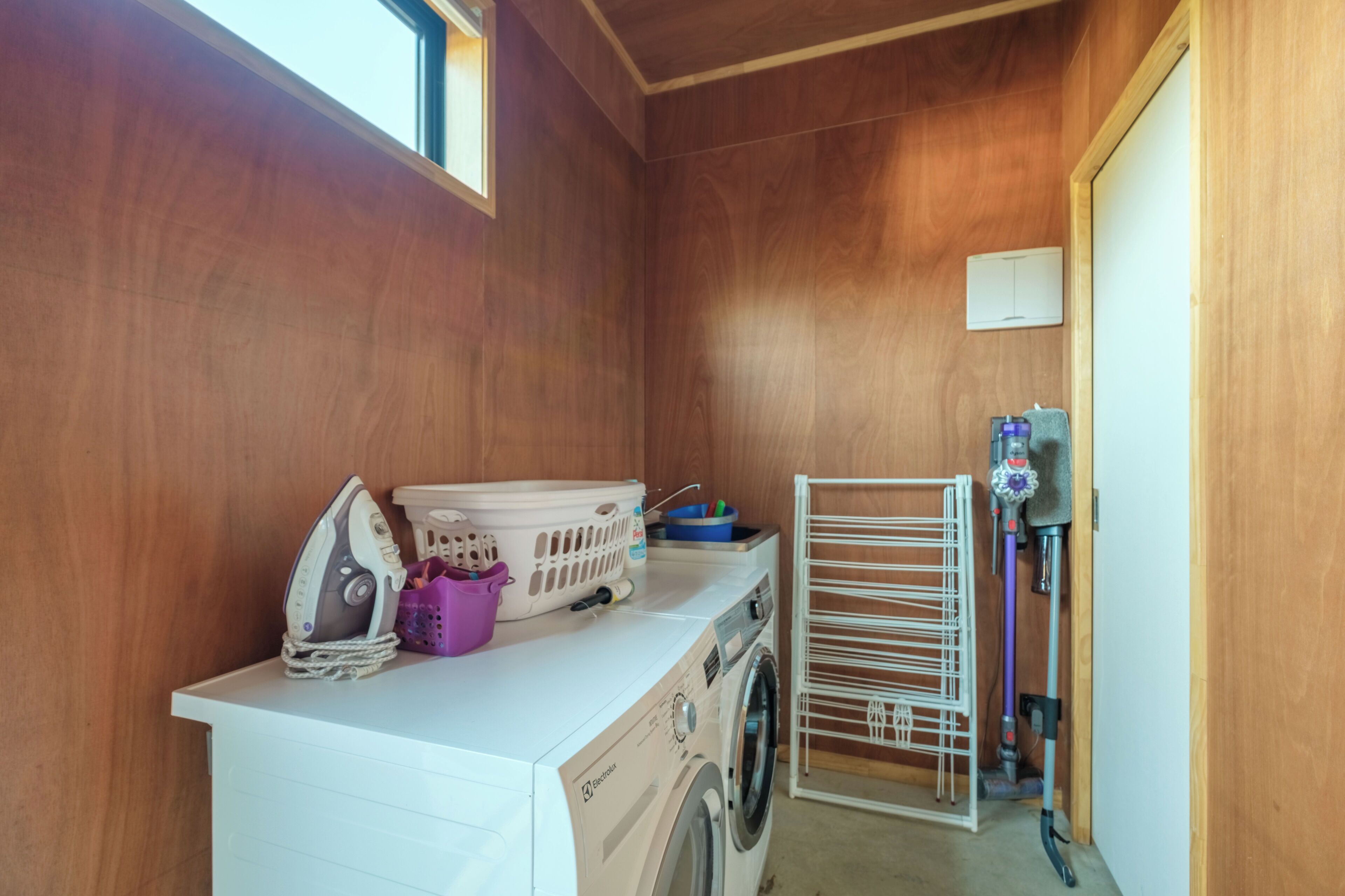 A laundry area with a washing machine, a drying rack, and a window providing natural light.