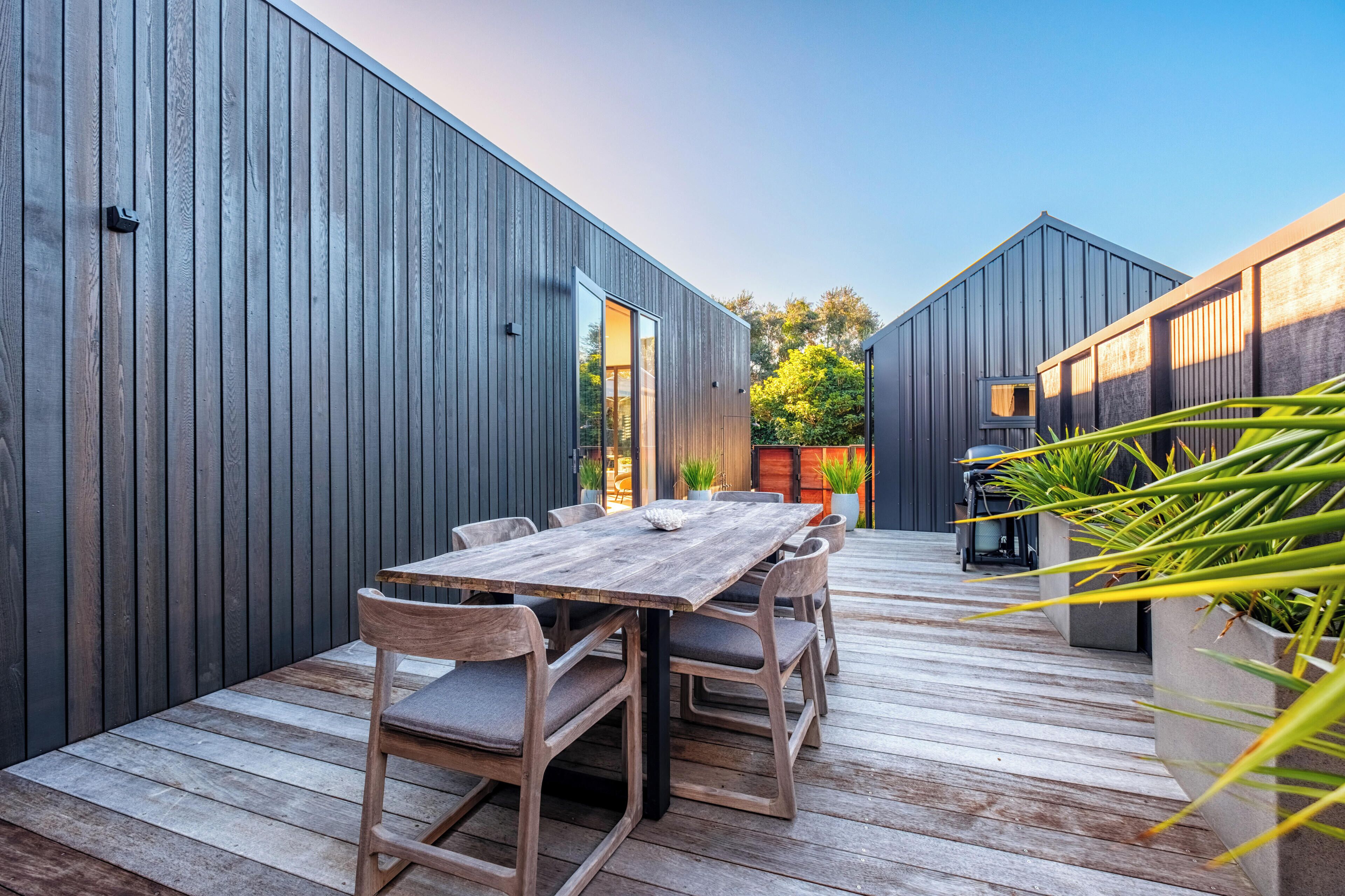 Una terraza de madera con una mesa y sillas, rodeada de paredes de madera oscura y plantas en macetas.