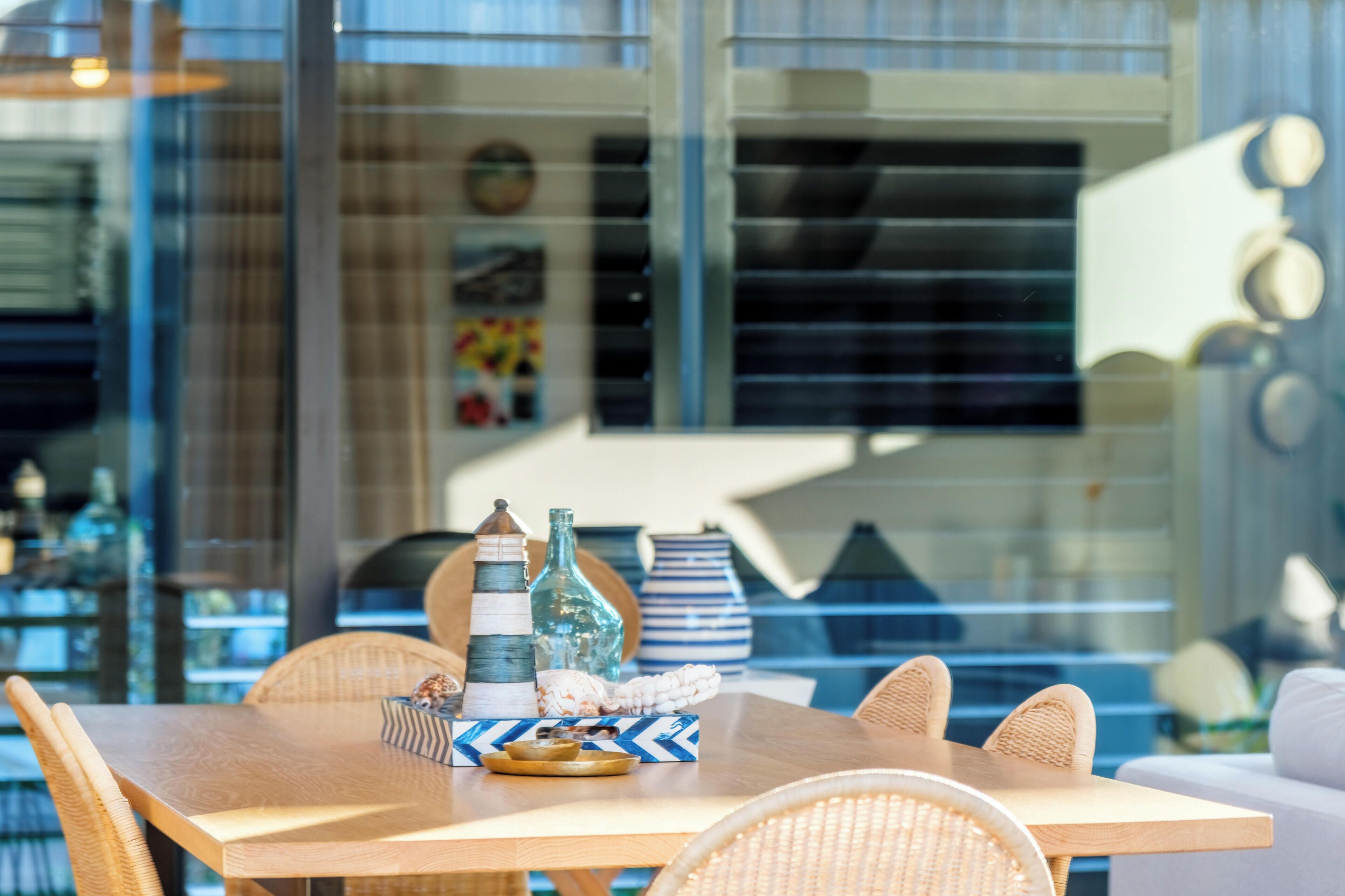 A dining area with a wooden table, wicker chairs, and decorative items including bottles and a striped vase.