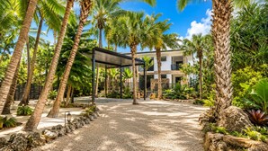 A modern building with a covered outdoor area, surrounded by palm trees and gravel paths.