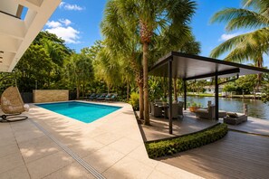 A pool area with a covered seating area, lounge chairs, and a view of a body of water. - Villa Sole Luxury Retreat – Upper East Miami (Miami)