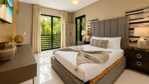A modern bedroom with a large bed, a nightstand, a lamp, and a view of greenery outside.