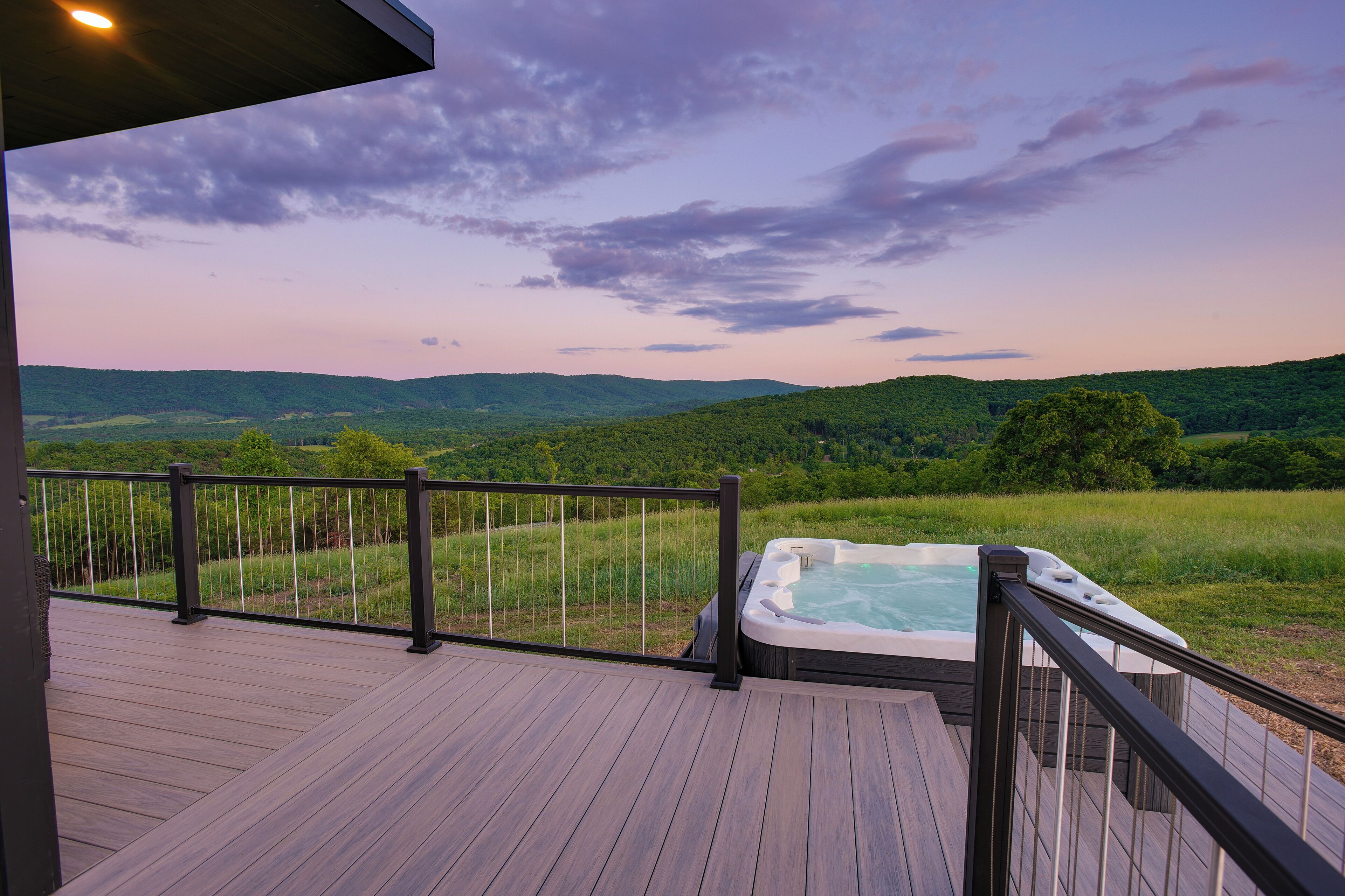 Eine Holzterrasse mit Whirlpool und Blick auf grüne Hügel.