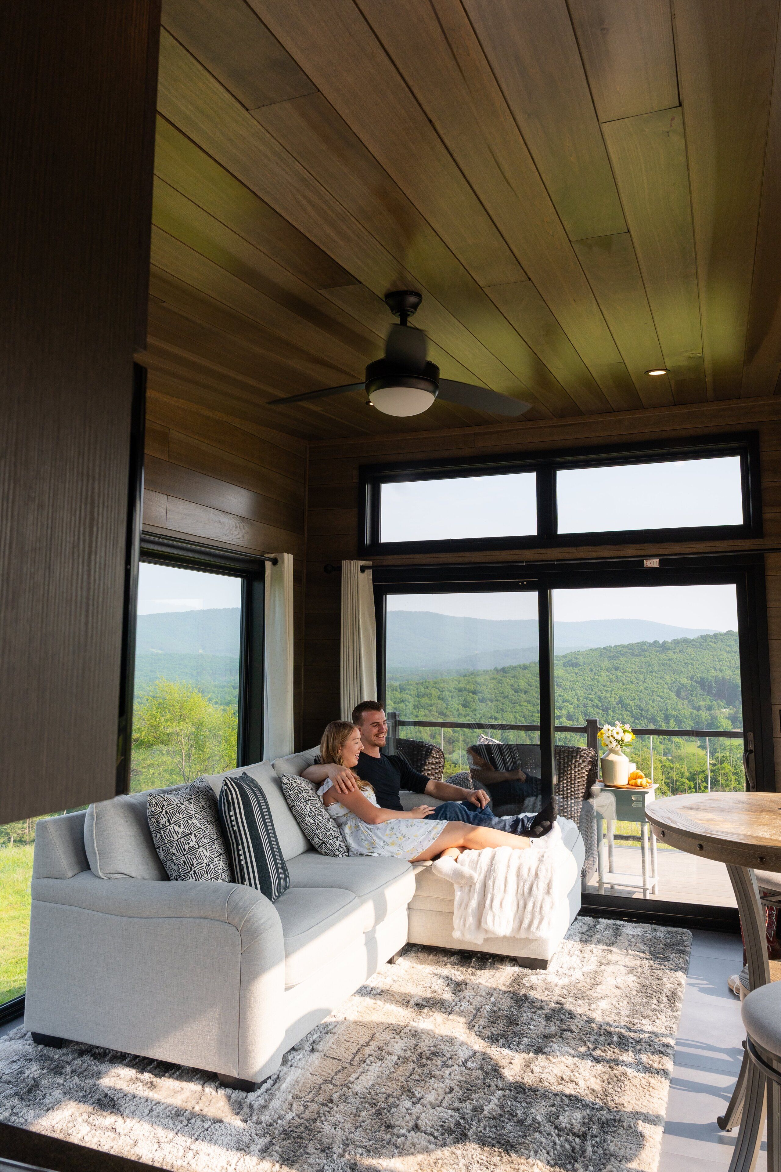 A cozy room with a large window, a sofa, a small table, and a ceiling fan.