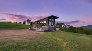 A modern house with a deck, large windows, and a hot tub. - Hart's Overlook | Hot Tub, Stunning Mtn Views + Private Pond! (Augusta)