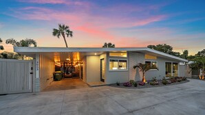 A modern house with a covered garage, a driveway, and a landscaped garden with palm trees and flowers. - The Palmy Pickle w/ Pickleball Court + Fire Pit! (Sarasota)