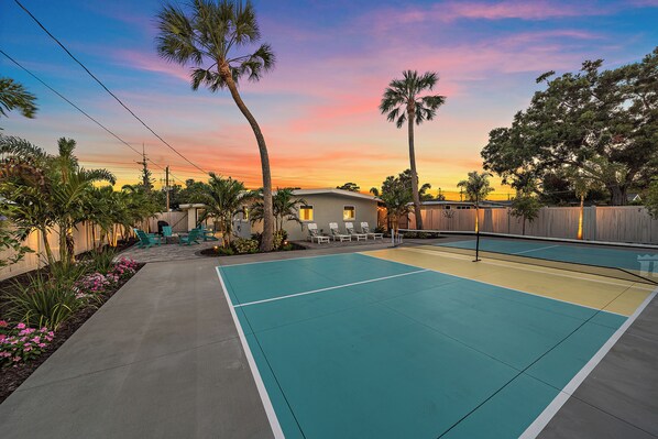 A tennis court with a wooden fence, palm trees, and a house in the background. - The Palmy Pickle w/ Pickleball Court + Fire Pit! (Sarasota)