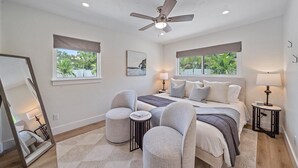 A bedroom with a bed, two bedside tables, a chair, a mirror, and a ceiling fan. - The Palmy Pickle w/ Pickleball Court + Fire Pit! (Sarasota)