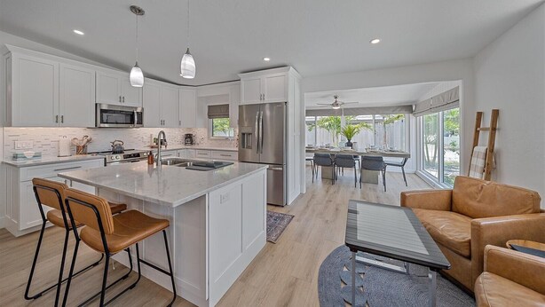 A modern kitchen with white cabinets, stainless steel appliances, and a central island with bar stools. - The Palmy Pickle w/ Pickleball Court + Fire Pit! (Sarasota)