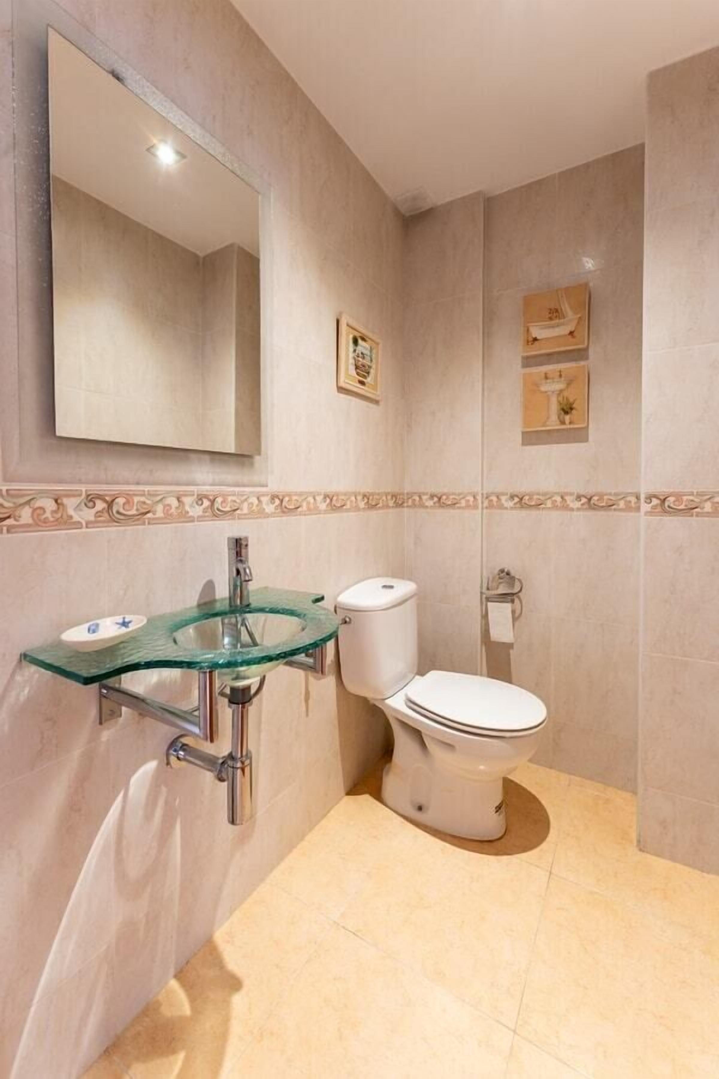 Une salle de bain avec un lavabo en verre, des toilettes et un miroir.