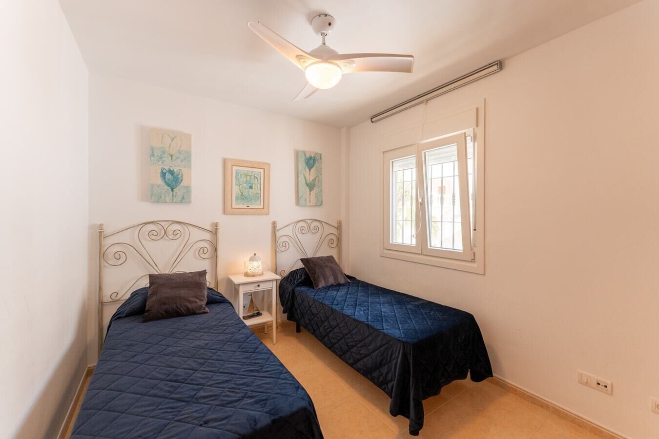 Ein Schlafzimmer mit zwei Betten, einem Deckenventilator, einem Fenster und Bildern an der Wand.