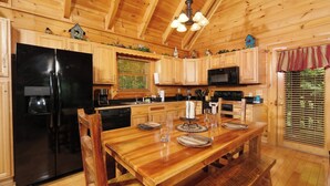 Interior de una cabaña de madera con una mesa de comedor dispuesta para cuatro personas, un refrigerador negro y un microondas.
