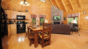 Interior acogedor de una cabaña con una mesa de comedor de madera, zona de cocina y chimenea de piedra.