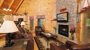 Una sala de estar acogedora con paredes de madera, una chimenea de piedra, sofás de cuero y un televisor montado sobre la chimenea.