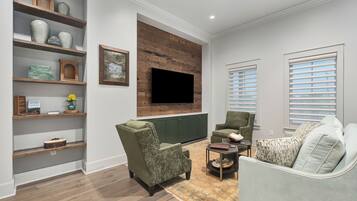 Una sala de estar con una unidad mural de madera, un televisor de pantalla plana, un sillón verde, un sofá gris claro y una alfombra estampada.