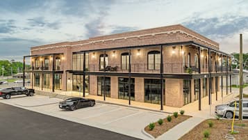 Un bâtiment moderne à la façade en briques et aux grandes fenêtres, doté d’un espace extérieur couvert avec des sièges et d’un parking.