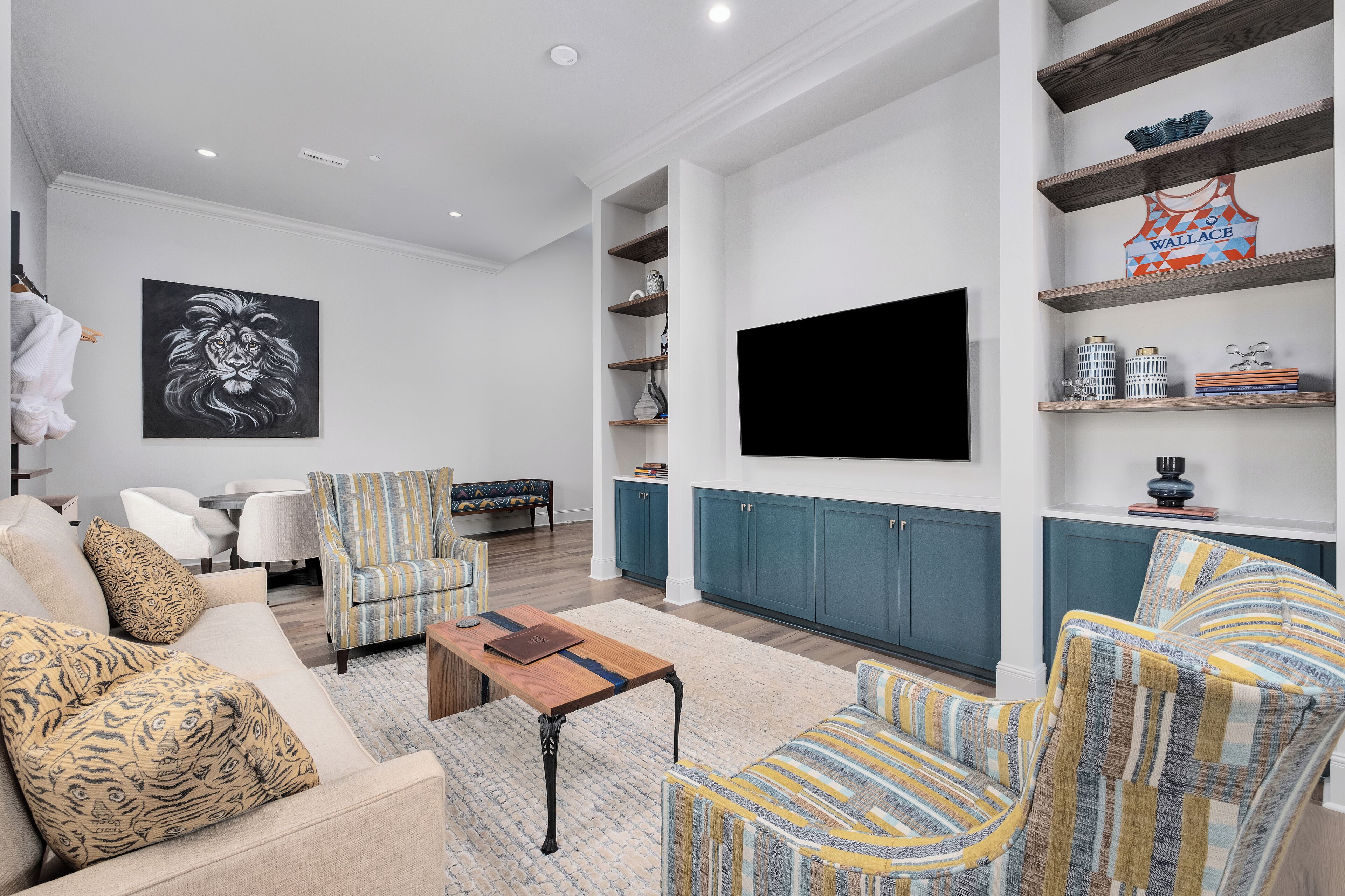 A modern living room with a sofa, armchairs, a coffee table, a TV, and shelves with decorative items.