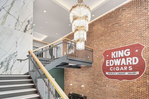Un escalier orné d’un lustre, un mur en briques et une enseigne indiquant « King Edward Cigars ».
