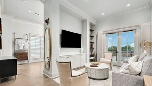 A modern living room with a flat-screen TV, wicker chair, grey sofa, and a round coffee table. - The Flying Fifty, a Luxury Boutique Hotel (Cullman)