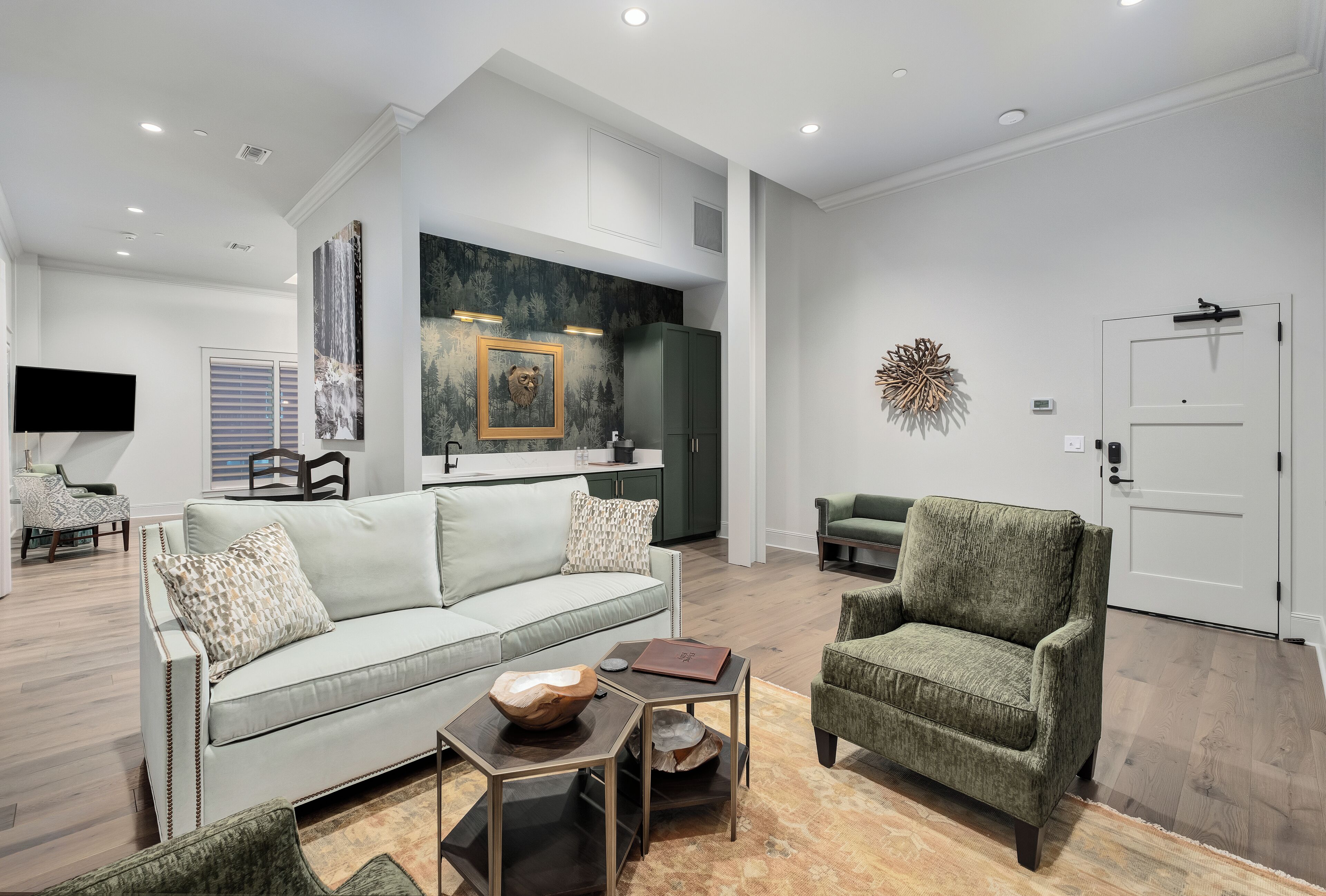 Un salon moderne avec un canapé, un fauteuil et une table basse. On aperçoit une cuisine à l’arrière-plan, avec un coin repas.