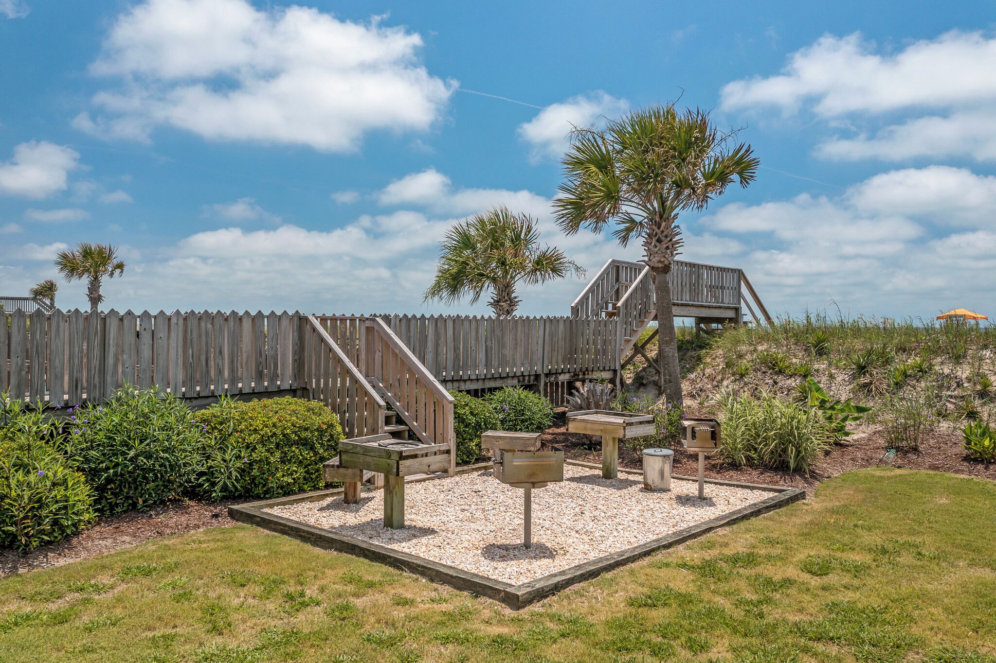 A wooden deck with a staircase leading to a raised platform, surrounded by gravel and greenery.