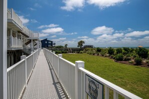 A white wooden deck with a "No Grills on Deck" sign, leading to a building with a blue exterior and a view of the ocean.