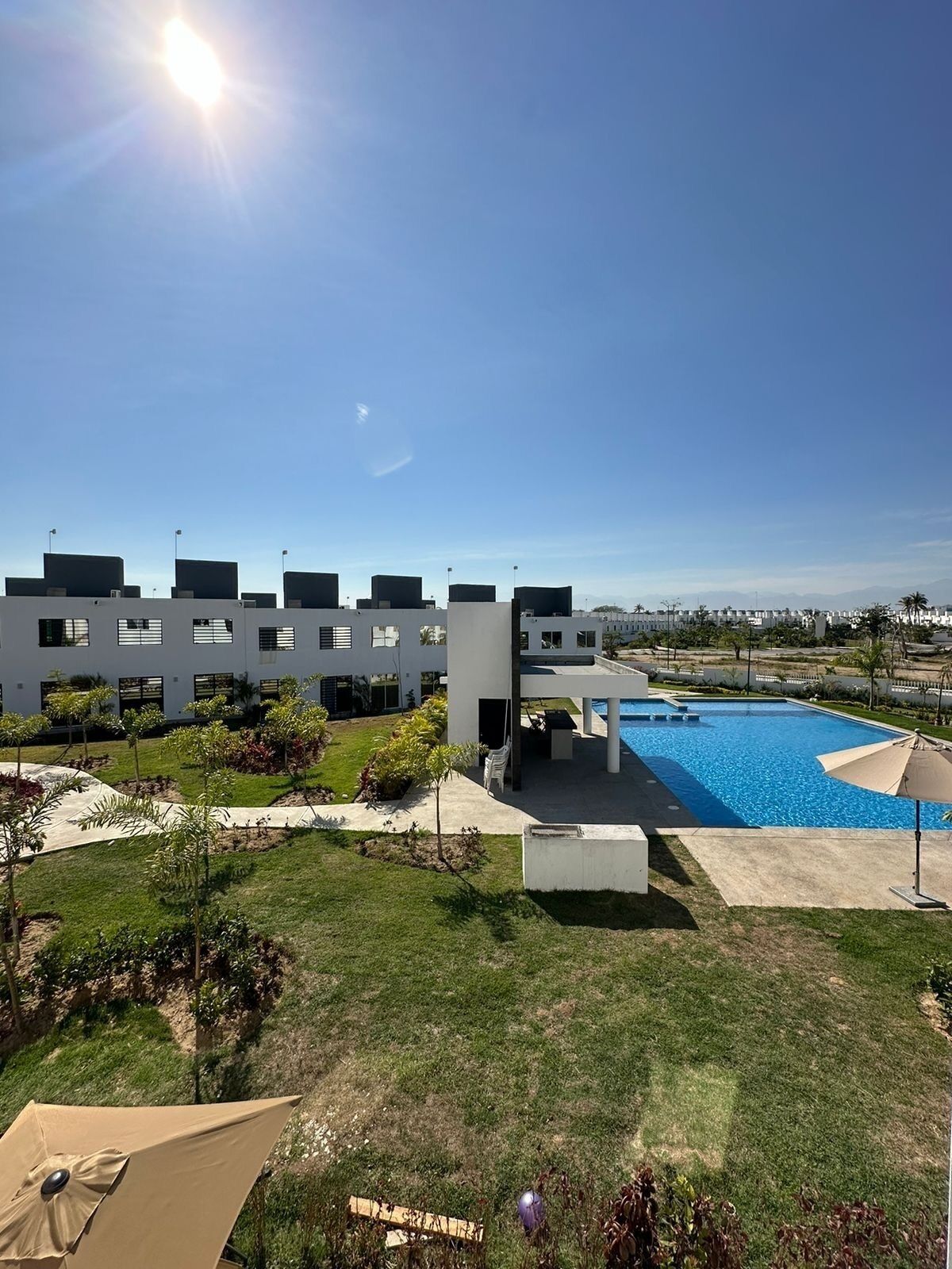 Un bâtiment moderne doté d’une piscine, entouré de pelouses bien entretenues et de petits arbres.