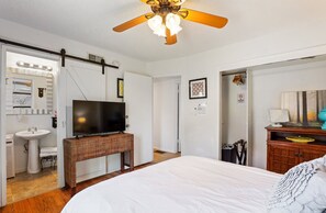 A hotel room with a bed, a television on a stand, a ceiling fan, a bathroom with a sink and mirror, and a door leading to another room. - Trinity Escape, Entire home, 3 bedroom, 2 bath near Lodi Lake (Lodi)