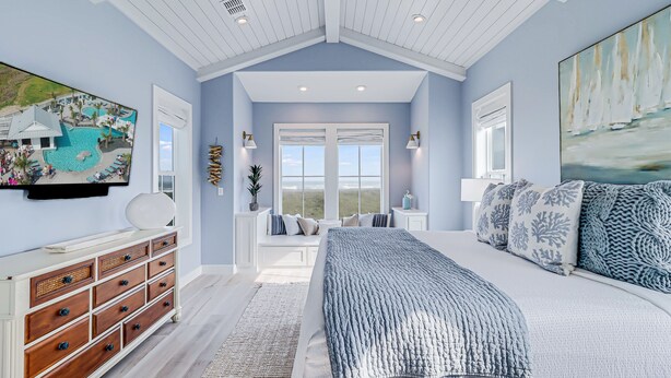 A bedroom with a large bed, a dresser, a window with a view, and a painting on the wall. - Newly built oceanfront home with elevator, balconies, and awe-inspiring views (Port Aransas)
