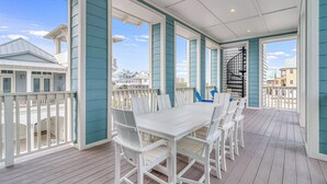 A covered outdoor area with a white table and chairs, teal walls, and a view of buildings in the background. - Newly built oceanfront home with elevator, balconies, and awe-inspiring views (Port Aransas)