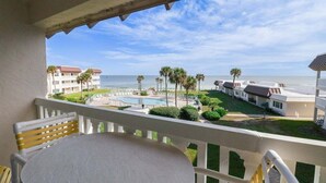 Ein Balkon mit Blick auf ein Schwimmbad, Palmen und einen Strand.