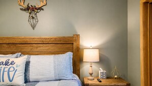 A bedroom with a wooden headboard, a bed with blue bedding, a nightstand with a lamp, a tissue box, and a remote control. - New Listing: On the Rocks in the Hideout (Lake Ariel)