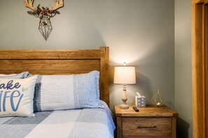 A bedroom with a wooden headboard, a bed with blue bedding, a nightstand with a lamp, a tissue box, and a remote control.