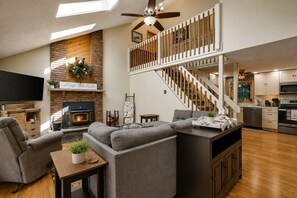 A spacious living area with a fireplace, a sofa set, a television, and a kitchen with modern appliances.
