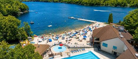A resort with a swimming pool, beach area, and a view of a lake.