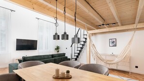 A modern living room with a wooden dining table, grey sofas, and a hammock. - Old Town Apartment with Mezzanine (Kraków)