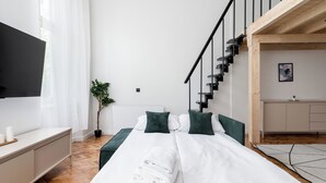 A modern hotel room with a large bed, a TV, a wooden staircase, and a small kitchenette. - Old Town Apartment with Mezzanine (Kraków)