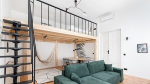 A modern loft apartment with a wooden floor, a green sofa, a dining area, and a black spiral staircase. - Old Town Apartment with Mezzanine (Kraków)