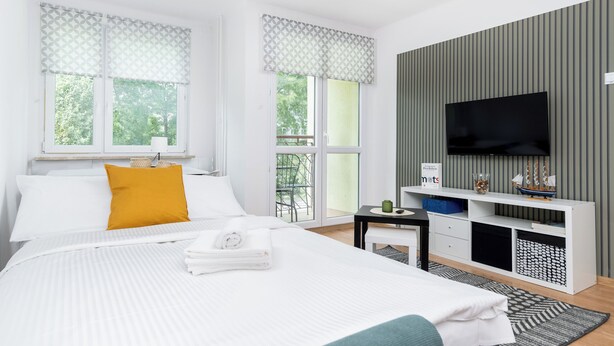 A modern hotel room with a large bed, a TV, a small desk, and a balcony view. - Olsza Comfy Apartment (Kraków)