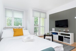 A modern hotel room with a large bed, a TV, a small desk, and a balcony view.
