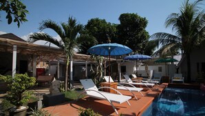 A poolside area with lounge chairs, umbrellas, and a statue.