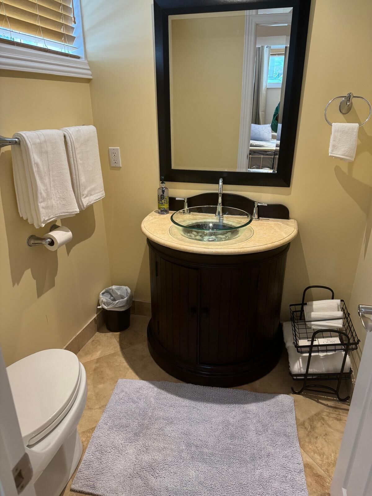 Un baño con un lavabo de vidrio, un inodoro y un espejo grande sobre el lavabo.