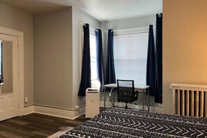 Een slaapkamer met een bed, een bureau, een stoel, een radiator en een raam met gordijnen.
