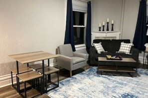 Een woonkamer met een bank, fauteuil, salontafel en een kleine tafel met stoelen.