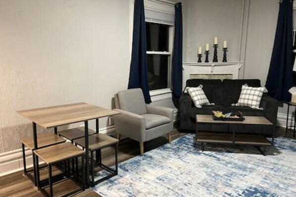 A living room with a sofa, armchair, coffee table, and a small table with chairs.