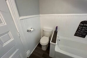 A bathroom with a toilet, a sink, and a bathtub. There is a sign on the wall with text.