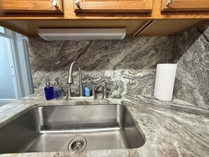 A kitchen with a stainless steel sink, marble backsplash, wooden cabinets, and a paper towel holder. - DM-C Comfortable 2BR Apartment (DuBois)